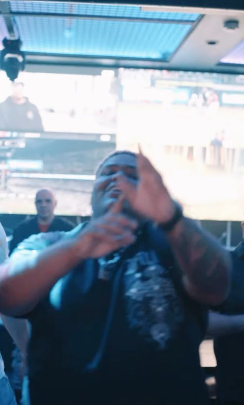 A frame from LMP's reel: a man in a black T-shirt gesturing at the camera in front of the bar's big screens