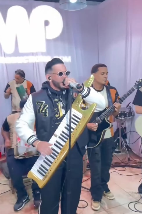 Joel El Insuperable singing and playing a gold keytar in front of the LMP backdrop