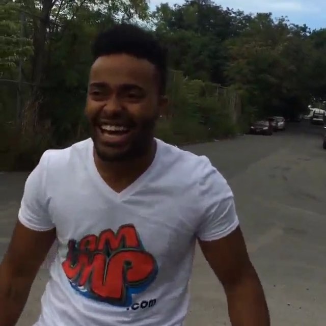Karlos Rosé laughing, in a white IAMLMP.com T-shirt, outdoors