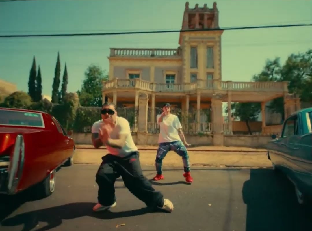 A frame from the “QUEMA” video in LMP's YouTube Short — the two dancing in the street beside a red lowrider